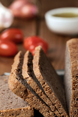 Gluten free buckwheat bread on a cutting board with tomatoes, onion and garlic on the background.