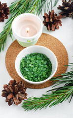 Small white bowl with green aroma bath salts (foot soak, epsom salts), burning candle and pine branches. Christmas aromatherapy. Winter spa and herbal medicine concept. Top view, close up, copy space.