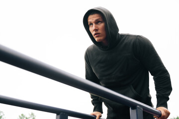 Athletic man young fitness trainer does exercises for triceps muscles. Bodybuilder is training on street fitness equipment, swing back