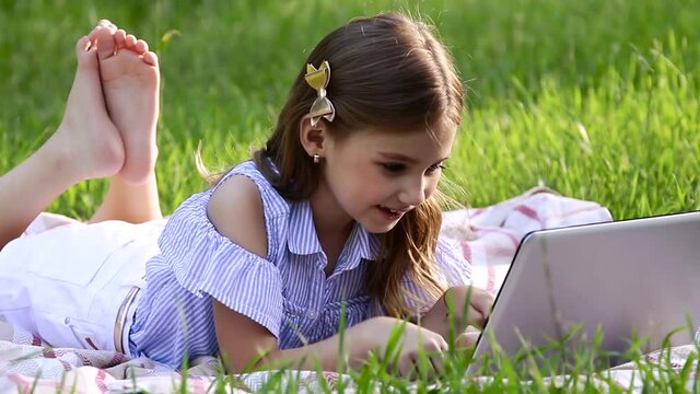 Caucasian pretty child with long hair looking at the laptop, lying on the blanket, texting email and watching at the camera. Concept of lifestyle and childhood.