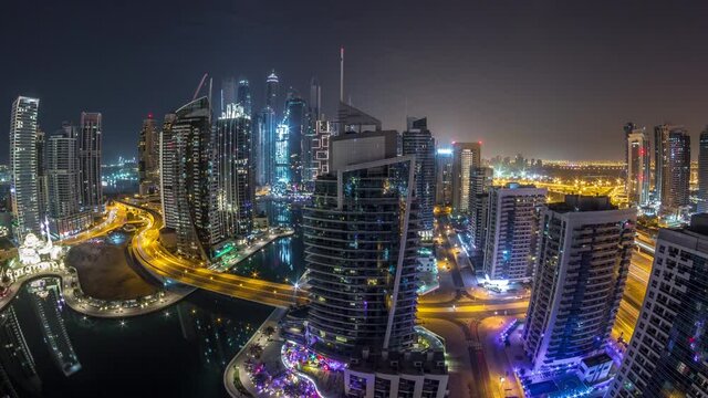 Aerial panoramic view of Dubai Marina residential and office skyscrapers with waterfront during all night timelapse with lights switching off. Floating boats and yachts