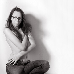 Sexy young woman wearing only jeans and glasses, she is hiding her breasts wirh her arms, monochrome photo