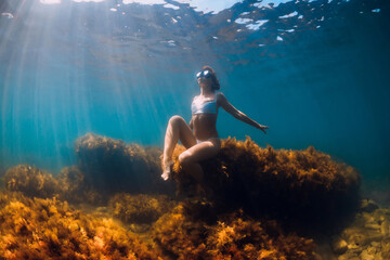 Woman freediver posing on stone with seaweed in underwater. Freediving in ocean