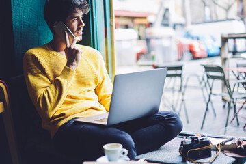 Confident creative manager of media marketing agency having phone conversation with executive manager discussing details of new startup project while sitting in coffee shop with free wifi zone