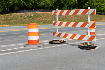 Traffic safety barricade and barrels with orange and white stripes on an asphalt street, horizontal...