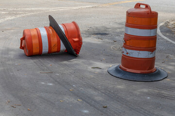 Two orange and white traffic safety barrels, one knocked over, metaphor for driving safety, danger and accidents, horizontal aspect