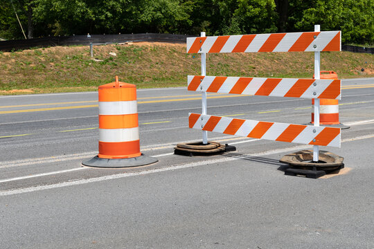 Traffic safety barricade and barrels with orange and white stripes on an asphalt street, horizontal aspect