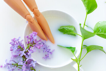 Obraz na płótnie Canvas doll legs in milk bath with lilac flowers. creative minimalistic concept of relax. top view.
