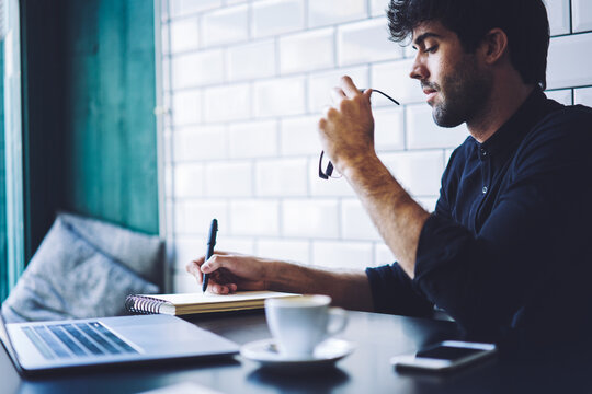 Young concentrated hipster guy creating article for personal website.Intelligent  bearded male preparing for upcoming quality control testing and solving problems writing report analyzing information