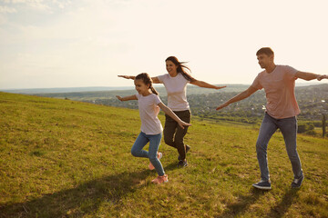 A positive family cheerfully runs across the field hands to the side in the morning at dawn in the sun.