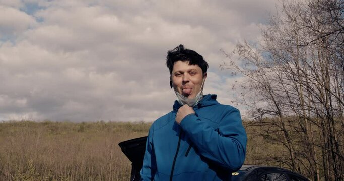 A man takes off his face mask and grimaces in front of the camera.