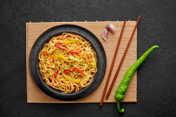 Chilli Garlic Hakka Noodles in black bowl on dark slate tabpe top. Indo-Chinese vegetarian cuisine dish. Indian veg noodles with vegetables. Classic Asian meal. Top view