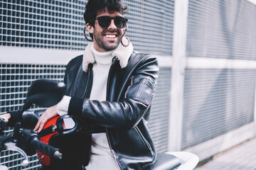 Positive handsome man in stylish sunglasses smiling away while sitting with helmet on...