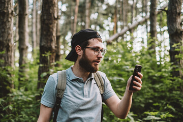 A young man using a smartphone in the forest. Tourism, active lifestyle.