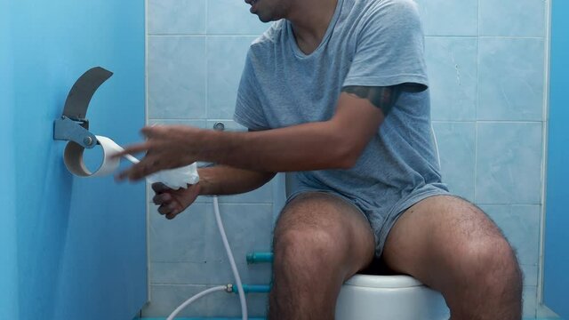 Young asien man retrieves some toilet paper to use after defecate In the bathroom