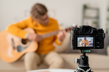 Naklejka premium Video-camera with contemporary young casual musician playing guitar on couch