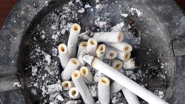 Concept for quitting smoking, no tobacco day, quitting addiction, anti-smoking campai. Ashtray filled with slim cigarette butts. Rotation 360 degrees Top view closeup.