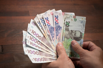 Male hands holding banknote fan. Caucasian man has pack of new Ukrainian hryvnias against of wooden...
