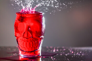 Red drink in an unusual circle in the shape of a skull with spray. Skull shaped glass with drink