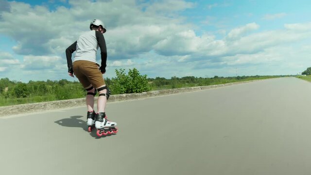 Young man on roller inline skates starting to roll on empty road on a sunny day