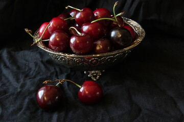 Fresh sweet ripe cherries on rustic plate on black background. Close up.