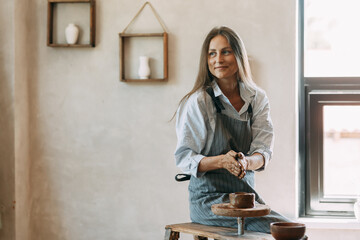 Beautiful inspirational sexy attractive pretty girl in jeans and shirt working in a workshop modeling on a potter's wheel handmade creativity art woman at work, hobby, girl painted with paint and clay © pavelvozmischev