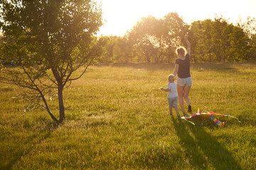 Mom with her little son fly a kite in the meadow, back view.