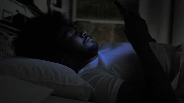 African Man Typing Message On Phone In Bed At Night