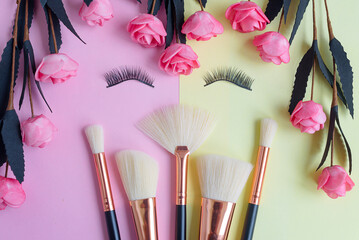 Obraz na płótnie Canvas premium makeup brushes and false eyelashes on a colored pink and yellow background, creative cosmetics flat lay