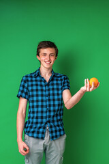 cheerful tall Caucasian teenager in checked shirt holds an orange in his hand.