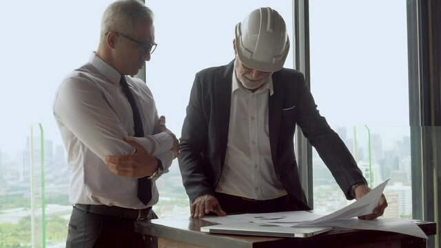 mature architect  talking with senior business manager or Project owner with plan to construction on tall building cityscape background