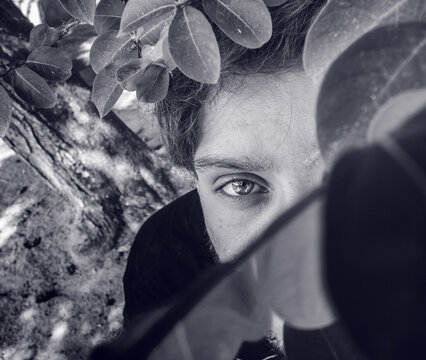 Man hiding behind leaves - attractive looks of a young man -  black white - secret emotions - happy and bright eyes 