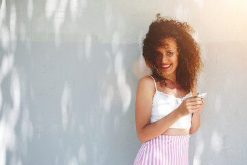 Half length portrait of beautiful hipster girl holding modern smartphone in hands while looking to camera. Copy space background for publicity content. Smiling young woman using cellphone application