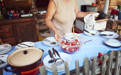 Woman preparing food and feast for summertime lunch at countryside rustic cottage outdoor kitchen.