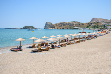 Fototapeta na wymiar Stegna beach with sunbeds and umbrellas, holidaymakers sun bathing (RHODES, GREECE)