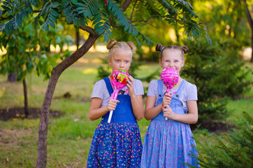 Two girls in denim sundresses play in the park with large lollipops