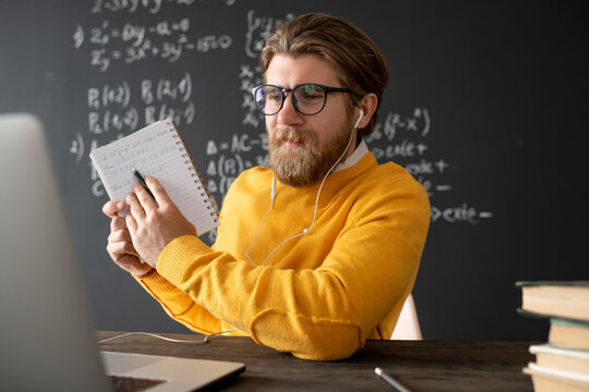 Confident teacher in eyeglasses and pullover pointing at his notes in copybook