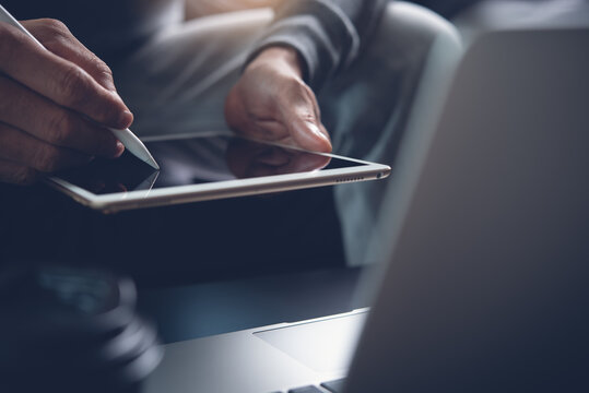Close up of man graphic designer hand using stylus pen on digital tablet working on laptop computer  at home