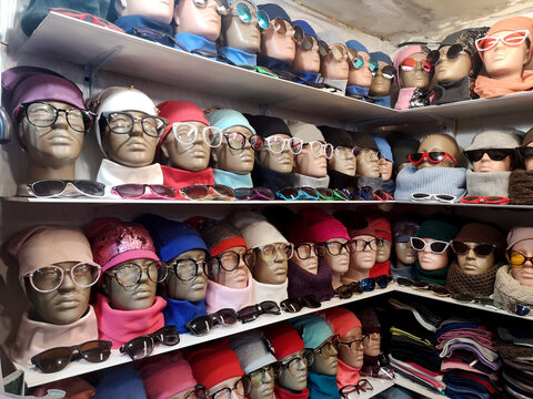 Many heads of mannequins are on the shelves dressed in colorful hats and glasses.