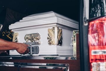 Close up of a casket loaded in a hearse or  funeral plan car or coach for the funeral procession. Selective focus.  - obrazy, fototapety, plakaty