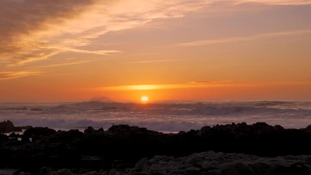 Slow motion Pacific Ocean big Waves rolling in and break on a rocky coast under a sunset sky at Pacific Grove, California on the Monterey Peninsula at stormy weather