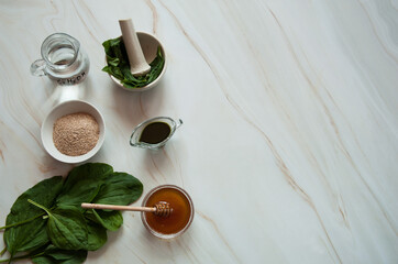 Natural home skin care. Ingredients of a face mask. Plantain leaf juice (Plantago major), honey, vodka and oat bran on a pastel green marble background. Free space.