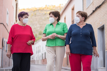 three older women walk down the street wearing a mask