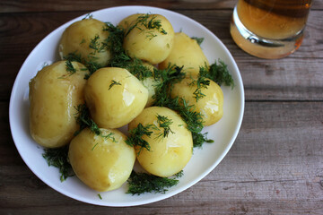 Traditional swedish midsummer food new potatoes with dill and light beer on old wooden board table. Whole boiled potatoes on the white plate

