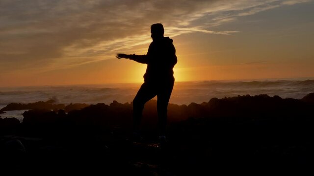 Men warrior monk practicing silhouette tai chi karate kung Fu on the rocky stones horizon at sunset or sunrise. Art of self-defense. Silhouette on a background of dramatic epic waves at pacific coast