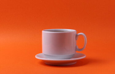 a white ceramic cup with black tea on orange background. minimalism style