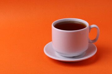 a white ceramic cup with black tea on orange background. minimalism style