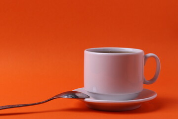a white ceramic cup with black tea on orange background. minimalism style