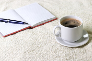black espresso in a cup and notebooks and a pen on light pastel tones background