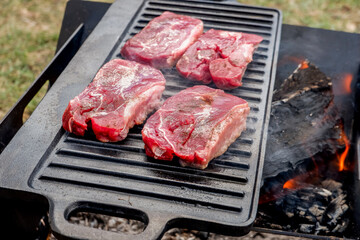 Beef steaks grilling on a cast iron plate on a camp fire. Campfire cooking. Outdoor BBQ.